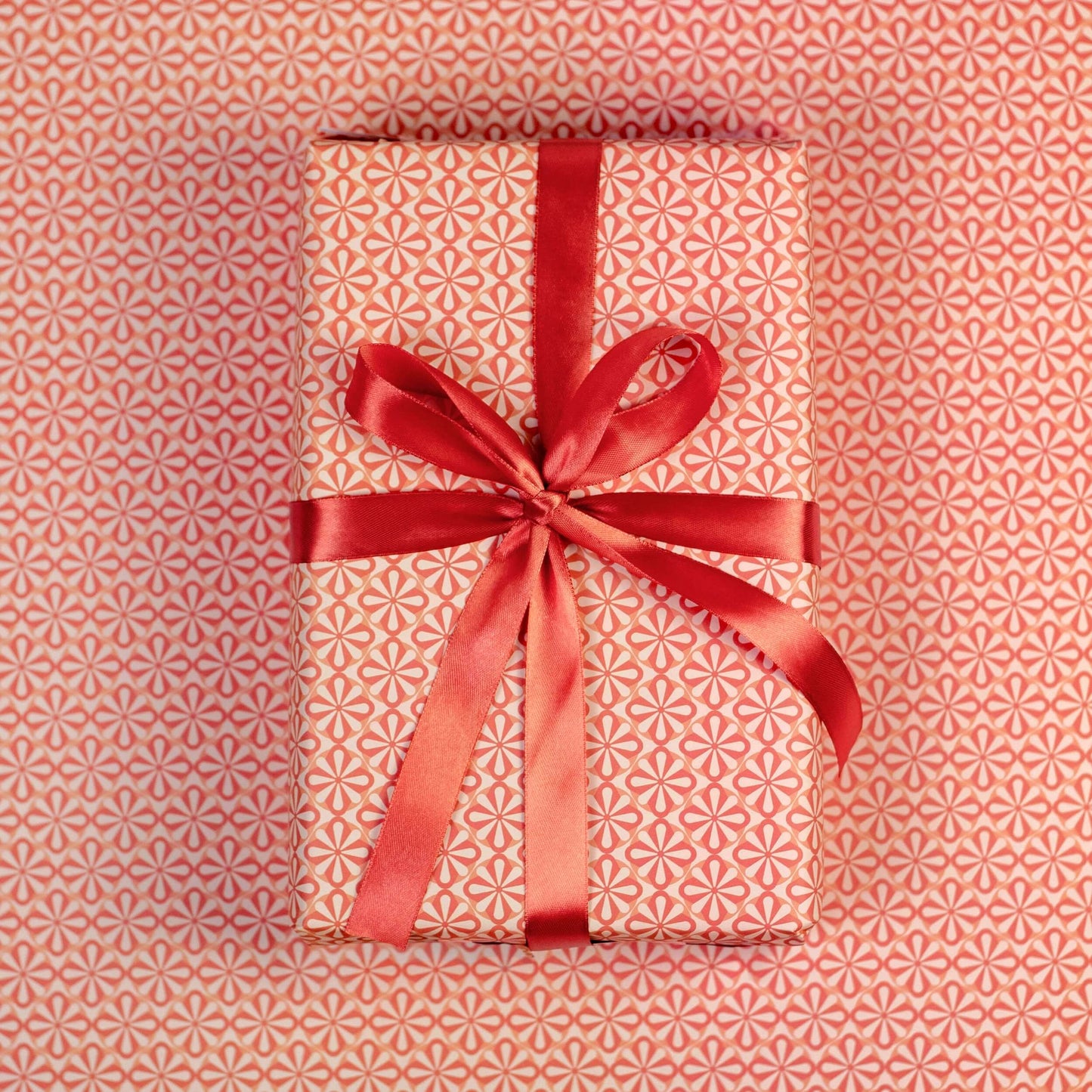 Gift wrapped in pink floral wrapping paper with red ribbon on a matching patterned background
