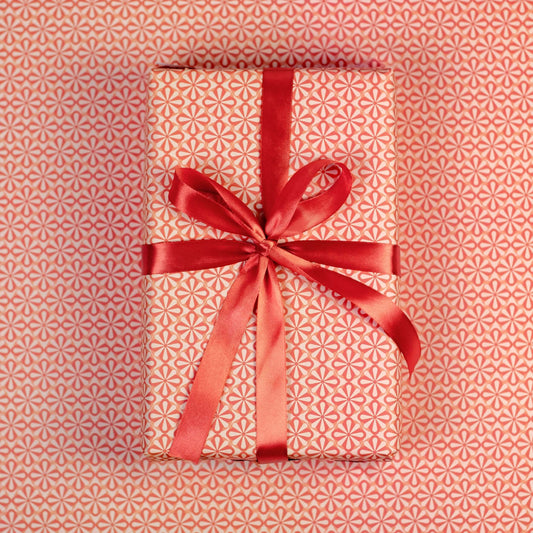 Gift wrapped in pink floral wrapping paper with red ribbon on a matching patterned background