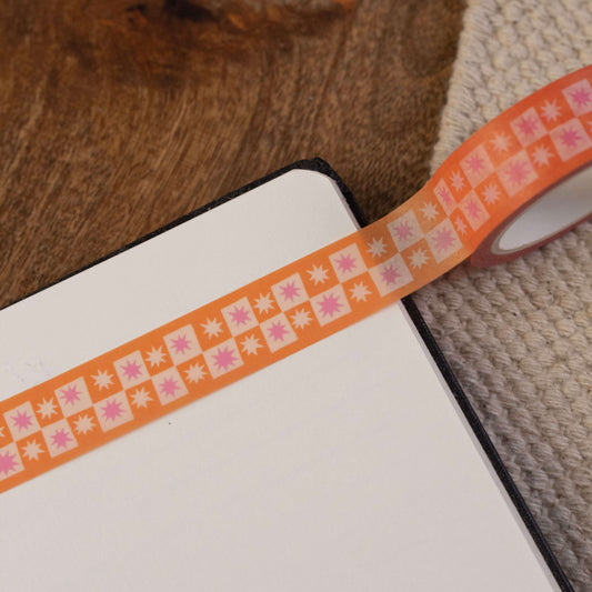 A washi tape stuck in a notebook. The washi tape has an orange and cream checkerboard pattern with 7-point stars in each of the checkers.