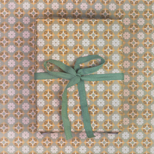 Gift wrapped in geometric floral patterned paper with a green ribbon on a matching patterned background