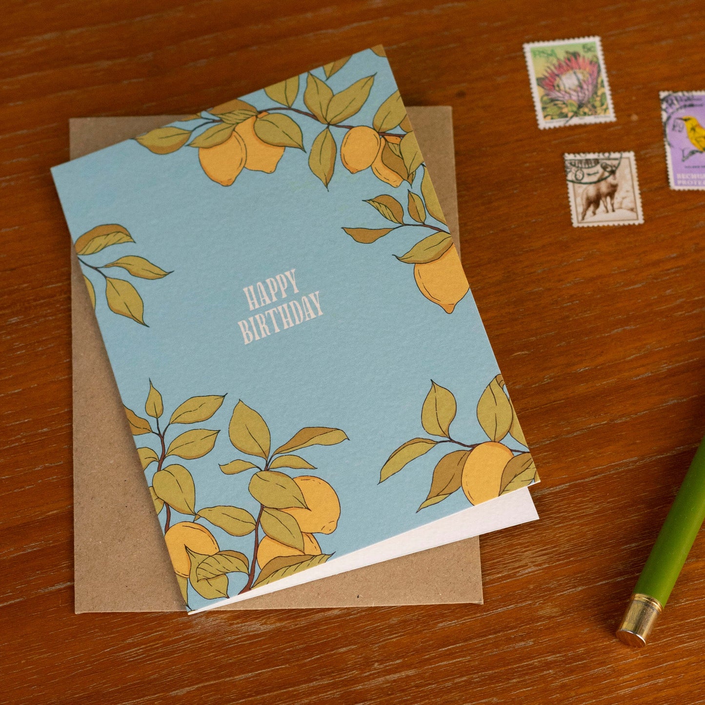 Birthday card with lemon design on a wooden surface with stamps and a pen.