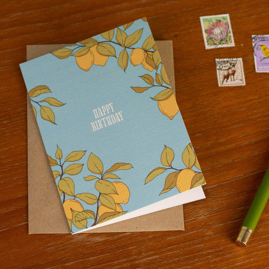 Birthday card with lemon design on a wooden surface with stamps and a pen.