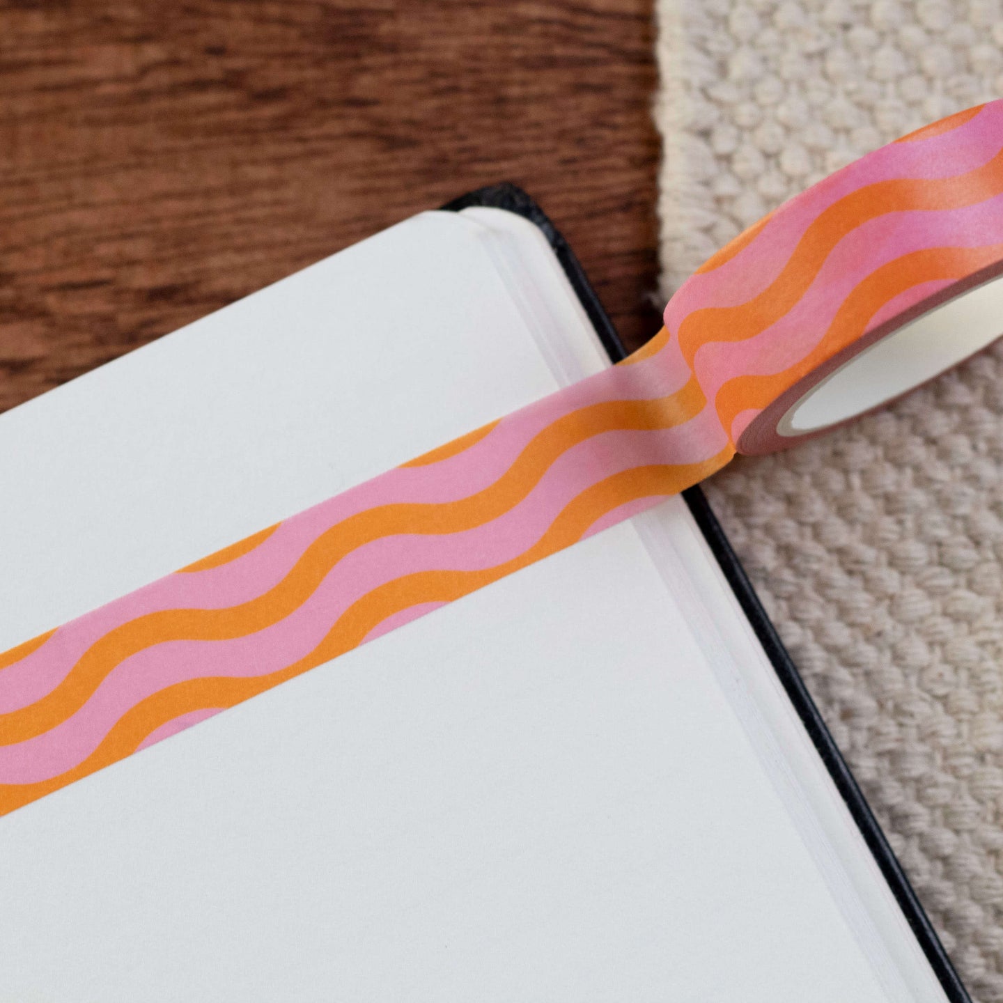 A pink and orange wiggle washi tape stuck in a notebook. The nootbook is sat on a brown wooden desk.